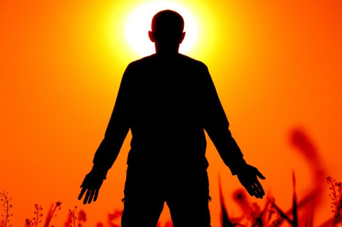 Silhouette of a man with arms at his sides facing the sun which is casting an orange glow around him